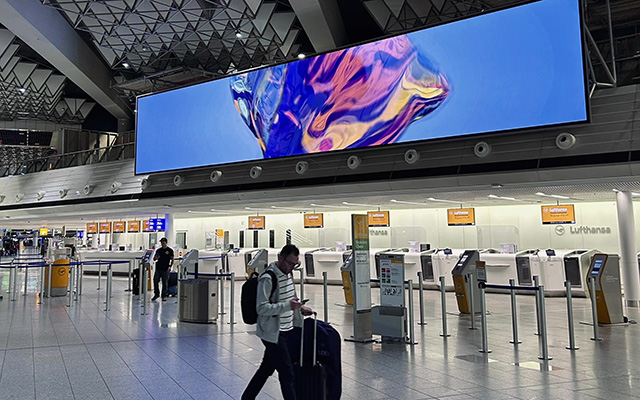 Airport check-in desks below a large wall mounted LED display